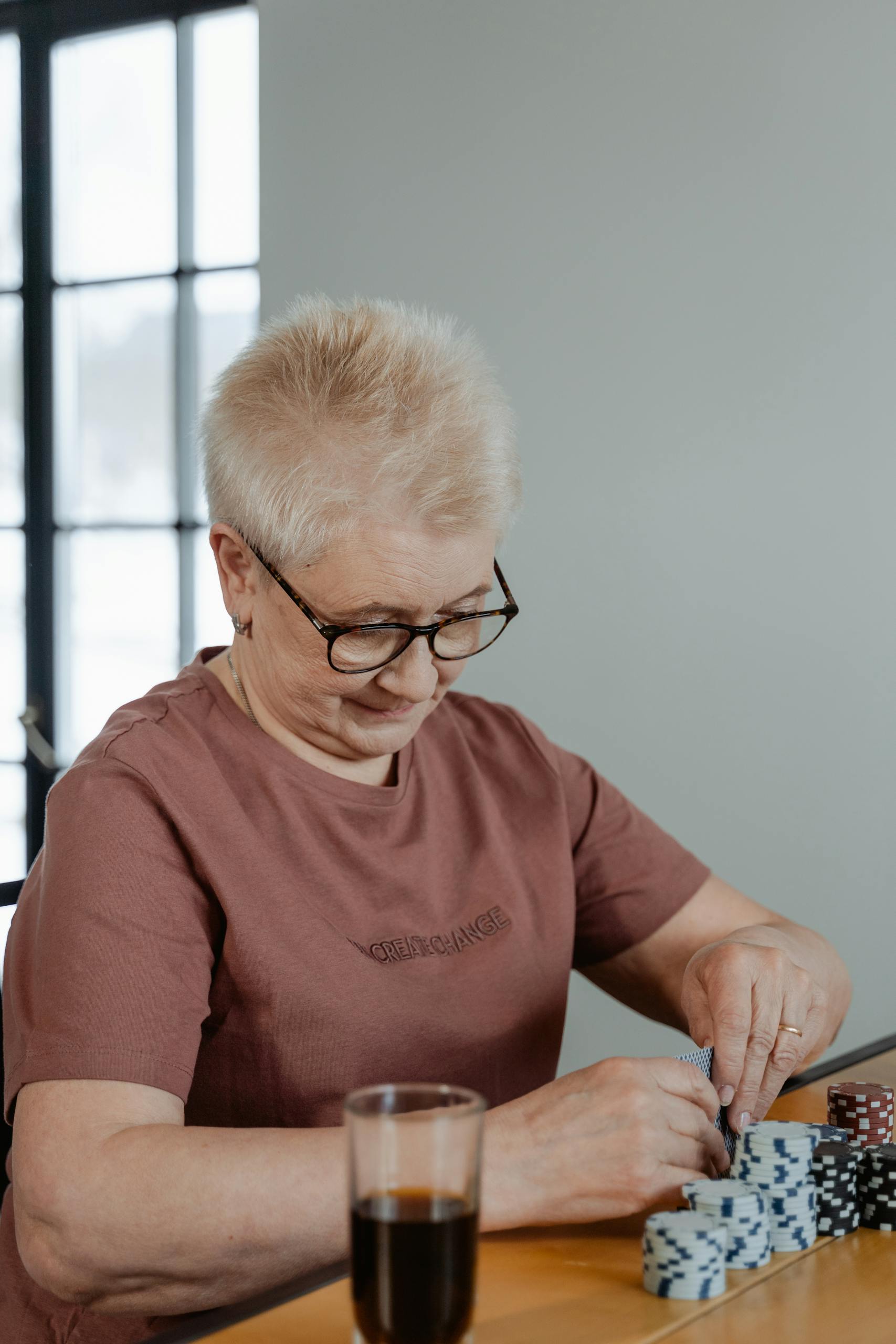 A senior woman enjoying a poker game at home, stacking chips with focus.